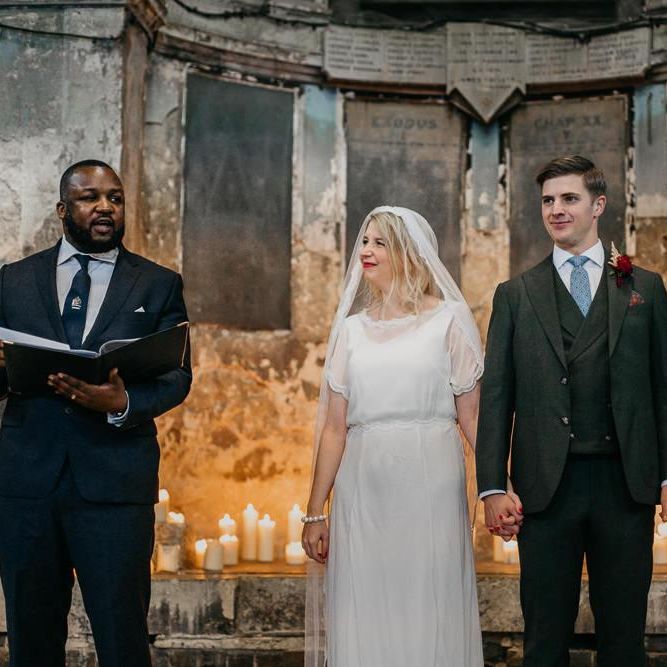 Bride wearing a  lace tipped veil with her groom at London wedding  with candle light backdrop