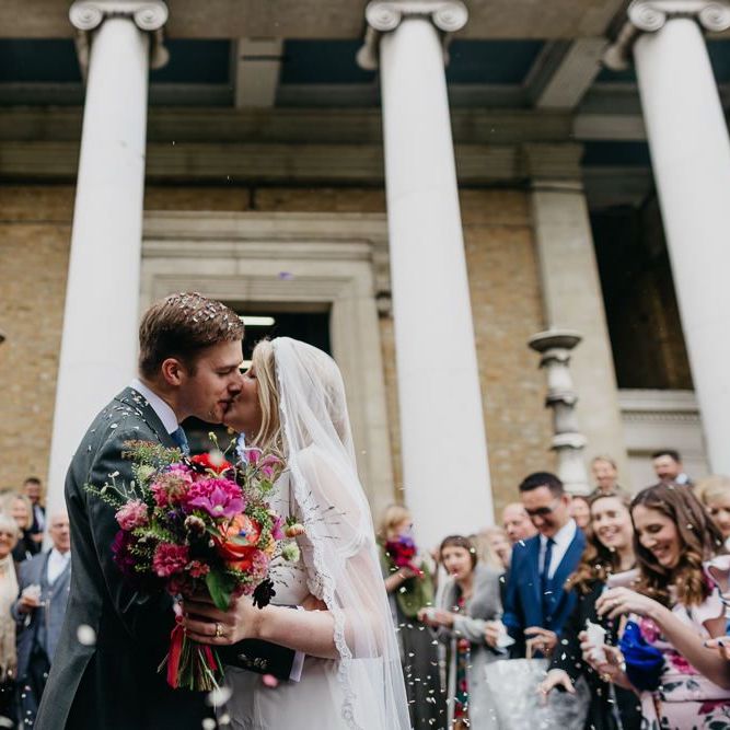 Bride and groom embrace with bright and colour bouquet for a fun and eclectic day