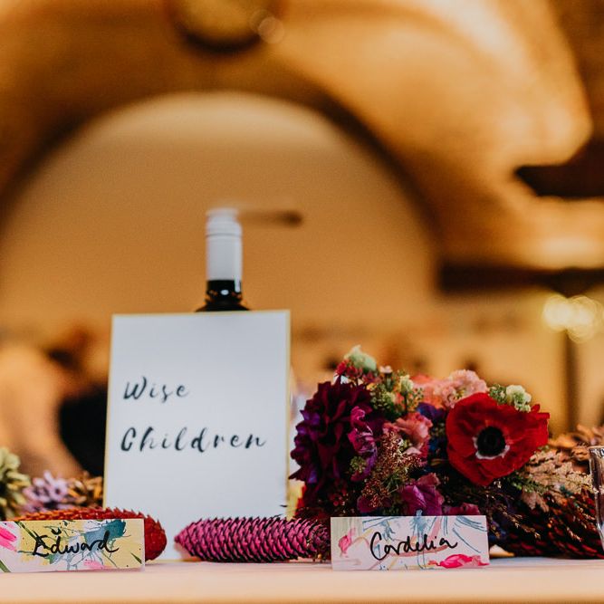 Hand painted watercolour place cards with pine cone wedding decor and bright flower arrangements
