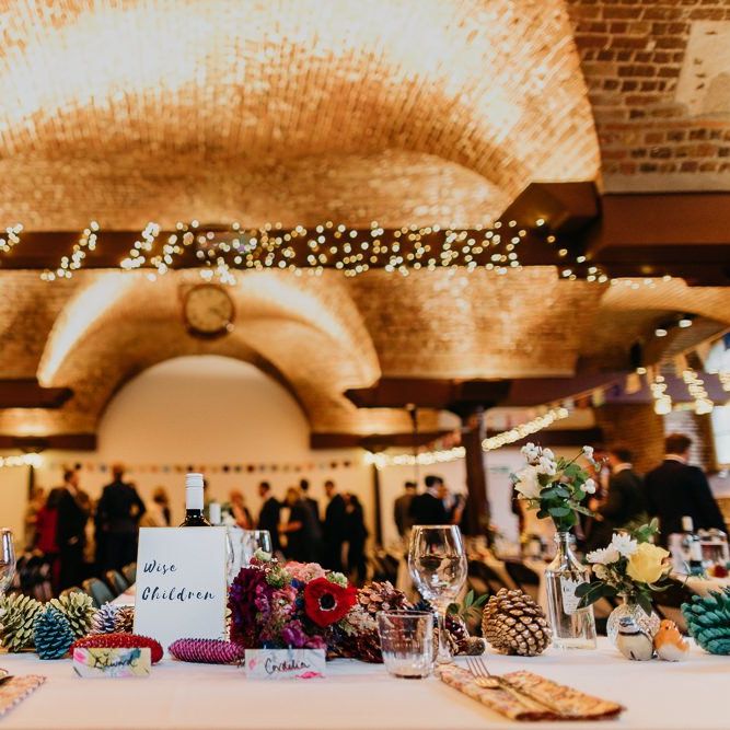 Hand painted watercolour place cards with pine cone wedding decor and bright flower arrangements