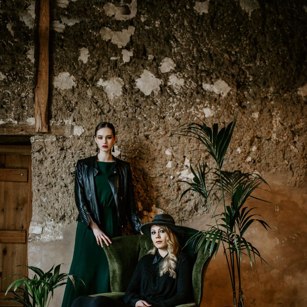 Green Velvet Chair | Botanical Plants | Bride in Black Dress &amp; Leather Jacket | Bridesmaid in Forest Green Dress &amp; Leather Jacket | Forest Green and Black Dark Decadence Wedding Inspiration in a Rustic Barn Planned &amp; Styled by Knots &amp; Kisses with Images by Daze of Glory Photography