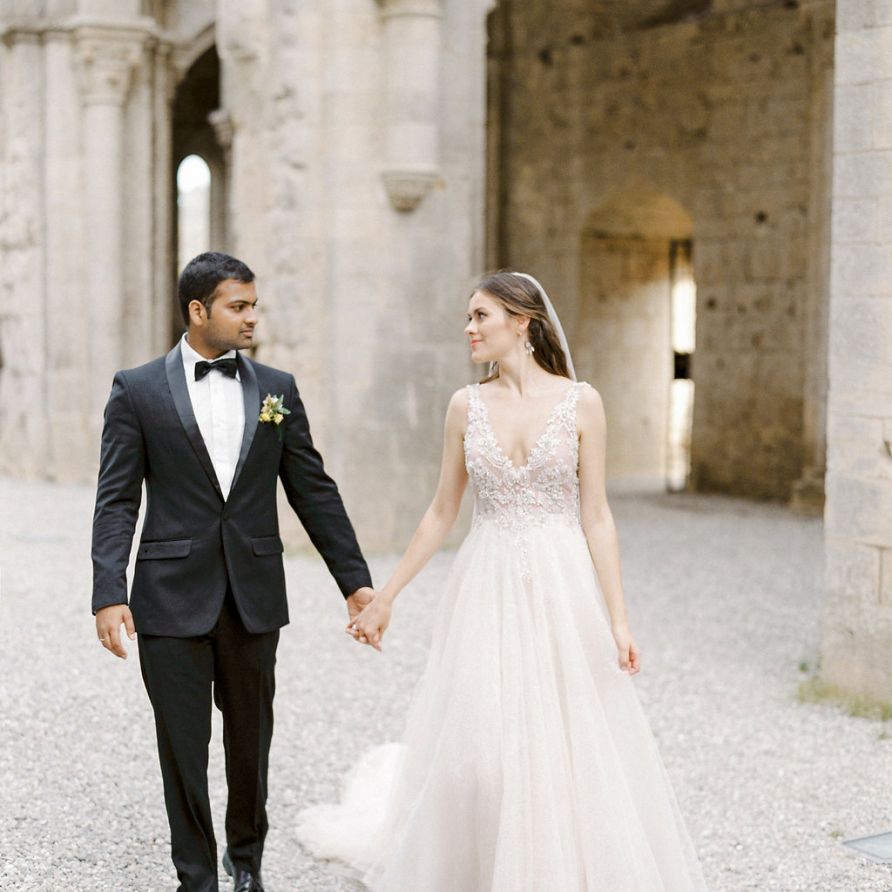 Bride in a Rara Avis Wedding Dress and Groom in Black Tie Suit Walking Through Their Open Air Church Wedding Ceremony Venue