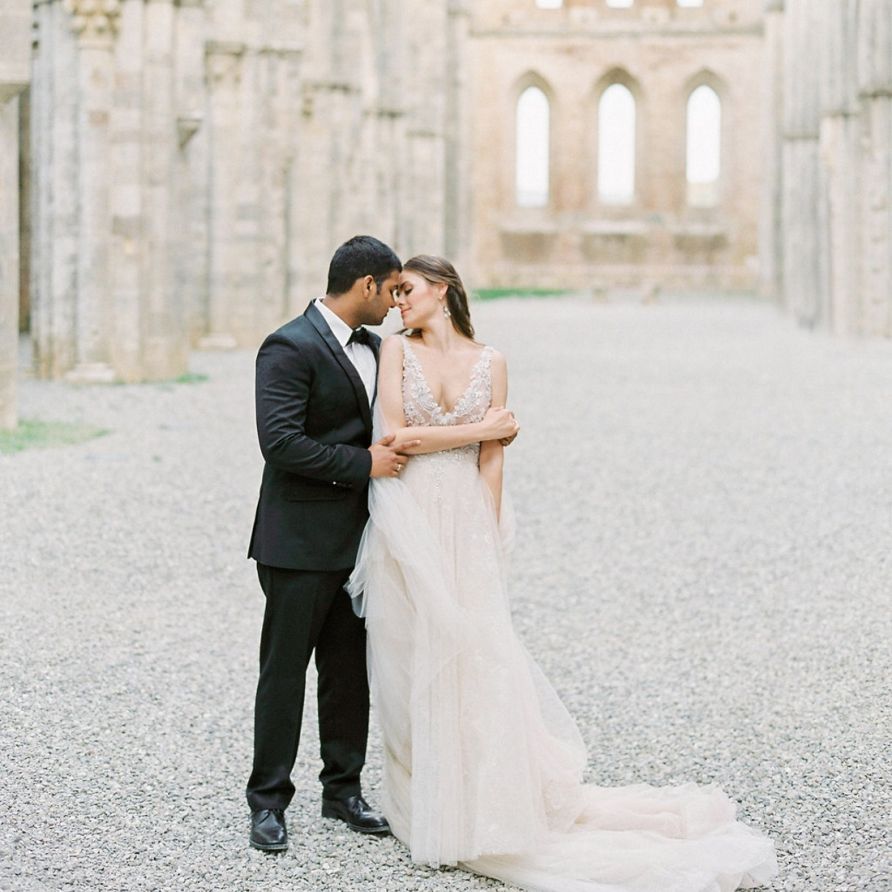 Bride in a Rara Avis Wedding Dress and Groom in Black Tie Suit Kissing in an Open Air Church Wedding Venue