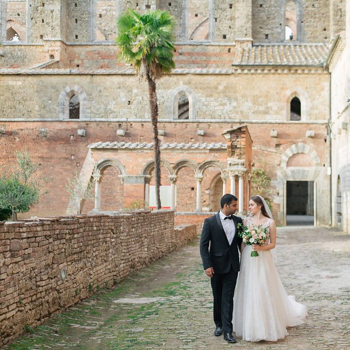 Bride in a Rara Avis Wedding Dress and Groom in Black Tuxedo Walking Through Their Historic Wedding Venue