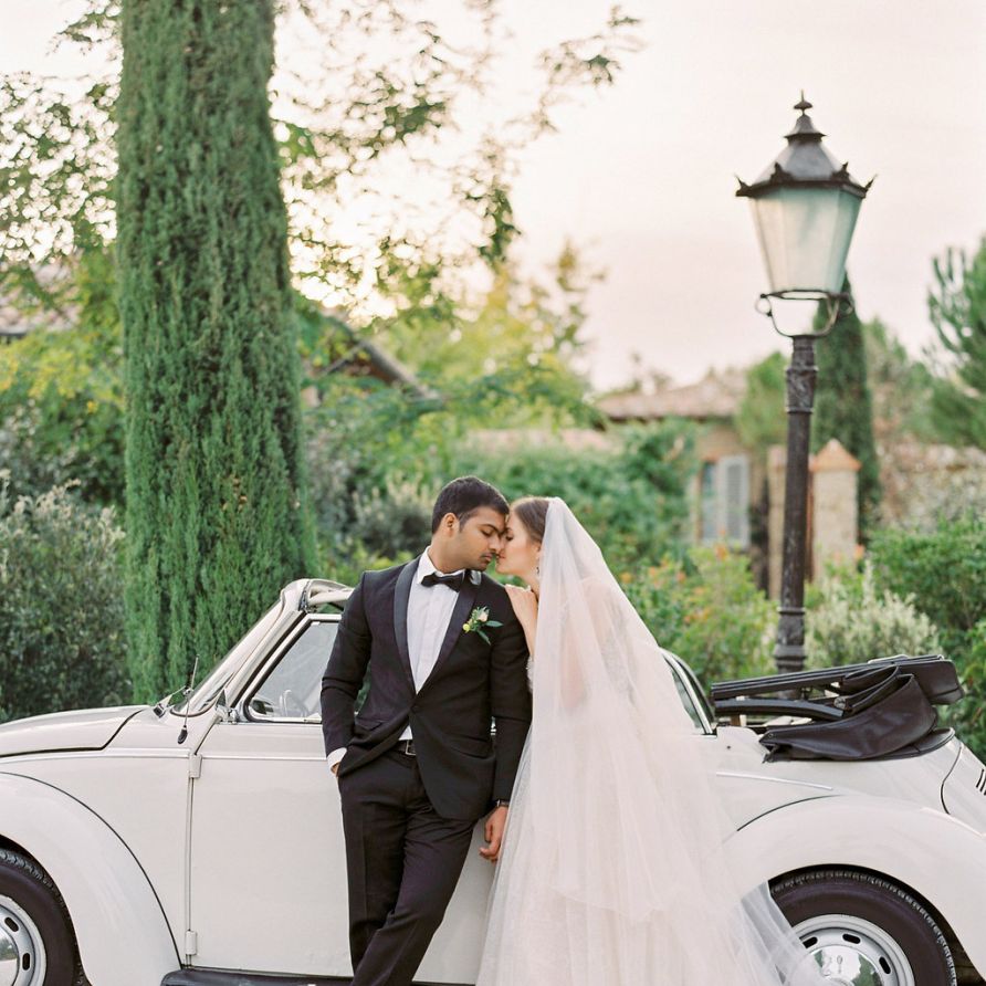 Bride in a Rara Avis Wedding Dress and Groom in Black Tuxedo next to their Convertible Beetle Wedding Car