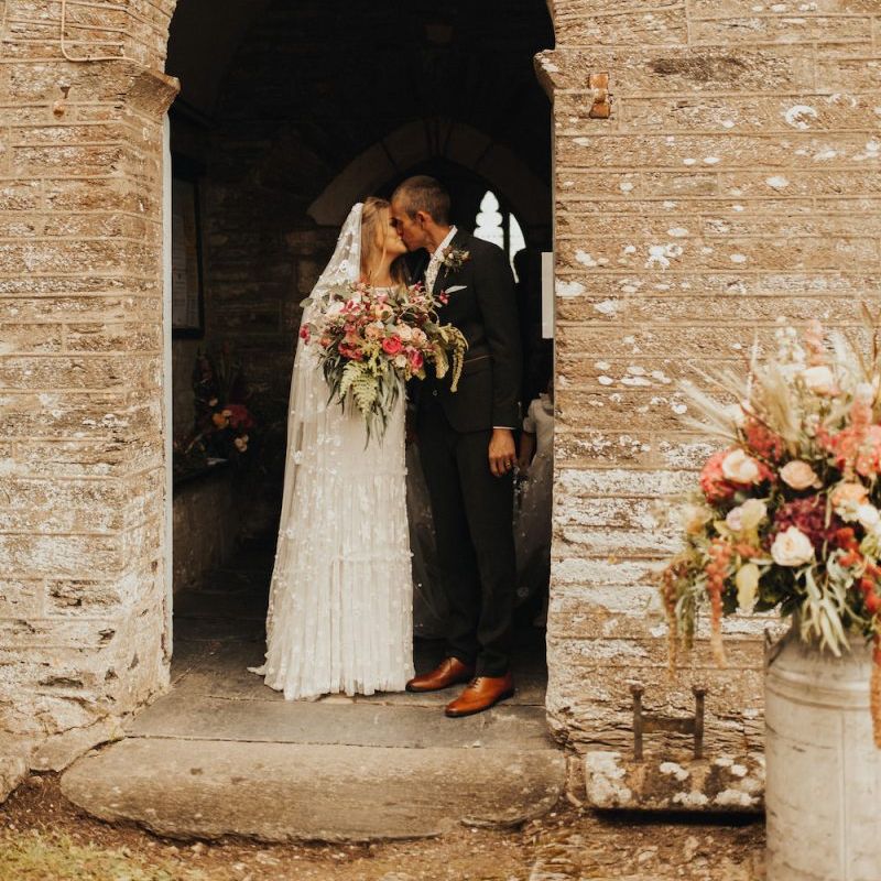 Bride in Eliza Jane Howell wedding dress kisses groom outside church