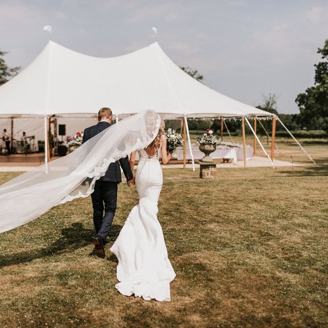 Bride in Pronovias Wedding Dress and Groom in Moss Bros Suit Walking Towards Tent Reception