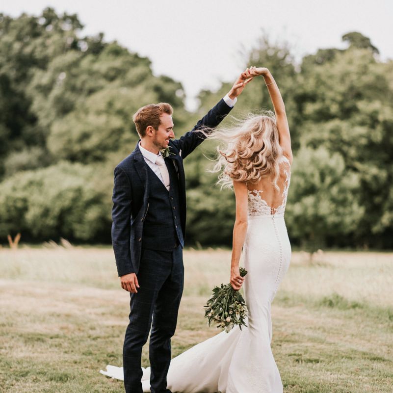 Groom in Navy Check Moss Bros Suit Twirling Bride in Vicenta Pronovias Wedding Dress