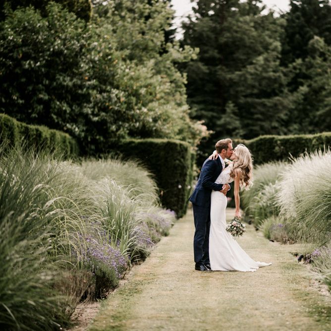 Bride in Vicenta Pronovias Wedding Dress and Groom in Navy Check Moss Bros Suit Kissing