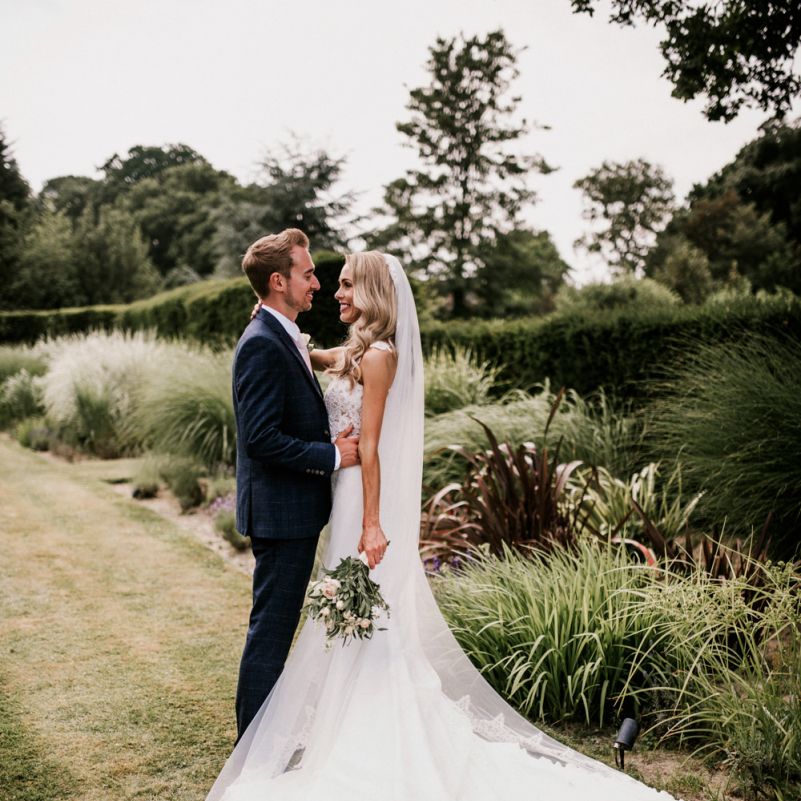 Bride in Vicenta Pronovias Wedding Dress and Groom in Navy Check Moss Bros Suit Hugging