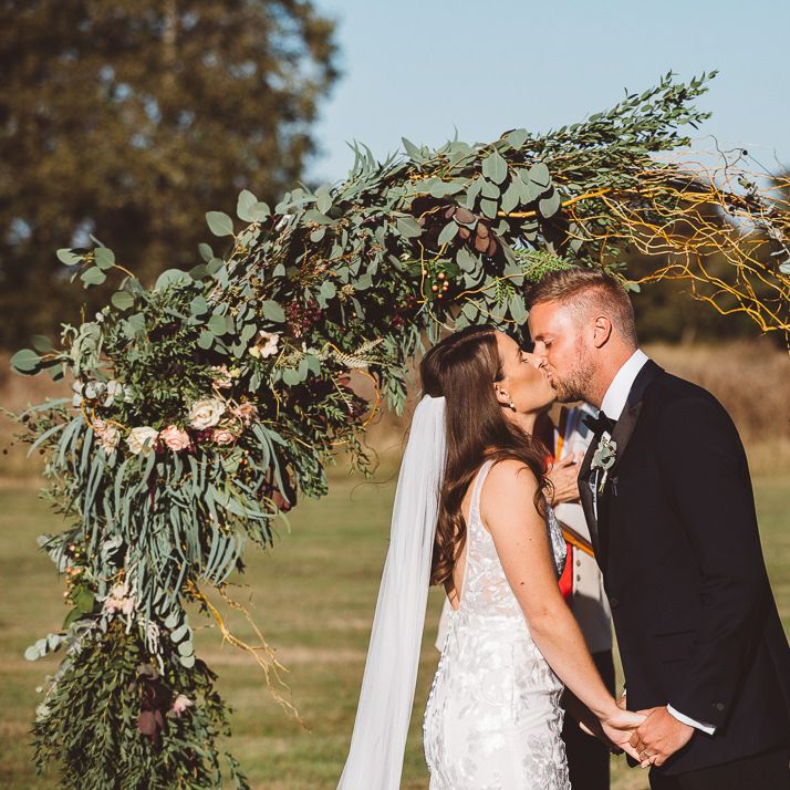 Bride and groom say 'I do' with foliage hoop decor for intimate outdoor ceremony