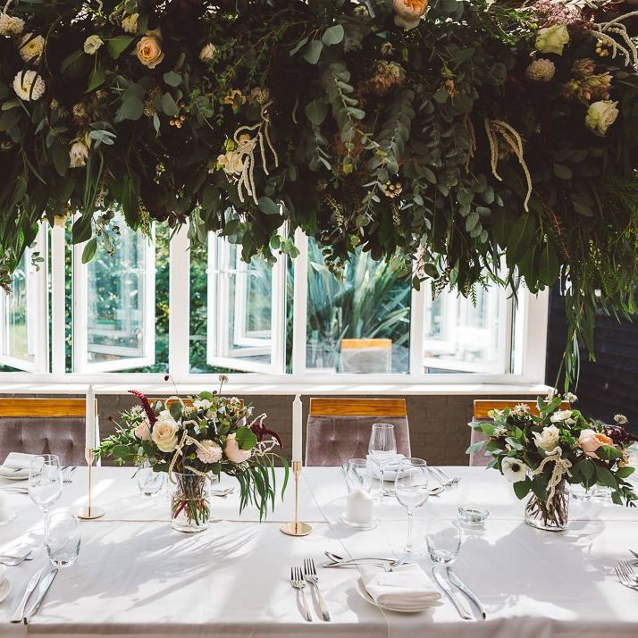 Hanging foliage and floral table arrangements styled with gold candlesticks for intimate and romantic wedding