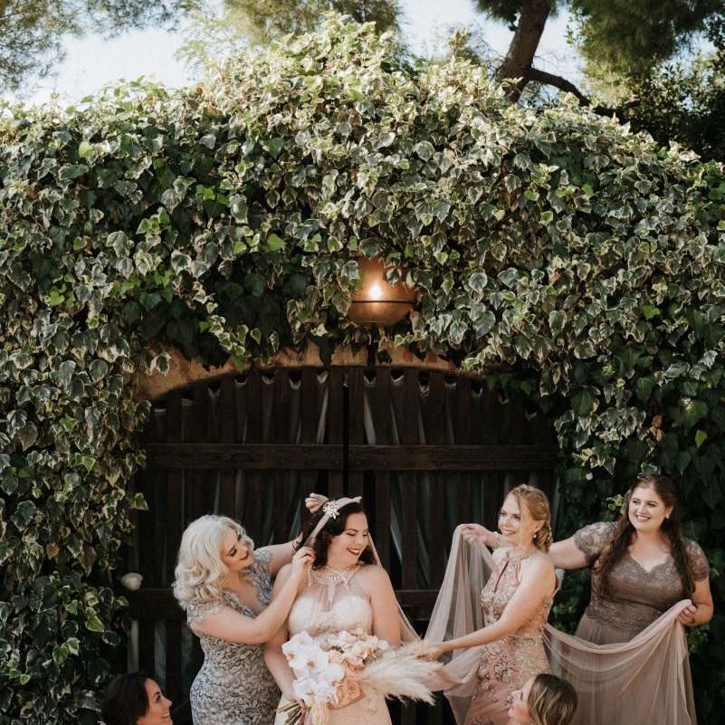 Bridesmaids tend to the bride who holds an orchid bouquet