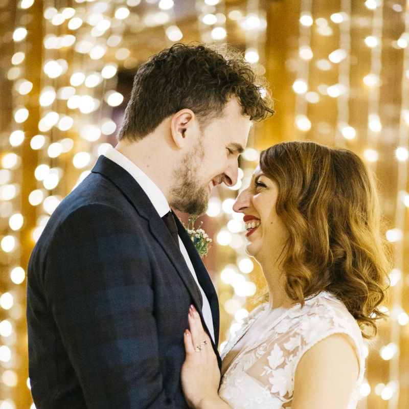Bride and groom embrace with fairy light backdrop