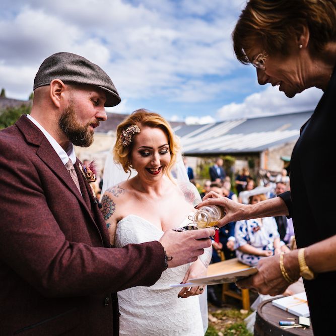 Wedding Ceremony | Bride in Strapless Sassi Holford Wedding Dress with Sweetheart Neckline | Groom in Burgundy Tweed Three Piece Suit | Edison Bulb Floral Installation at Kingsthorpe Lodge Barn Wedding | Johnny Dent Photography