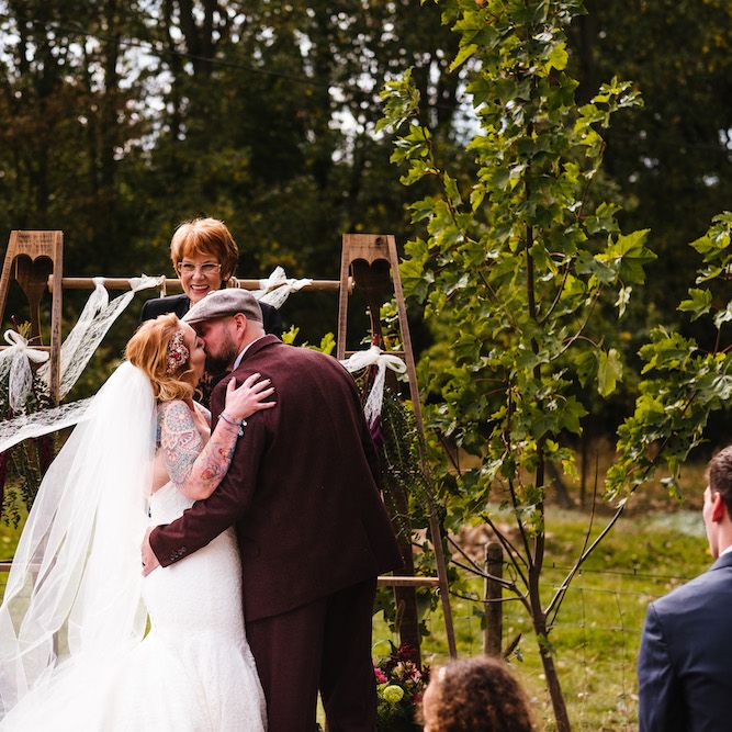 Wedding Ceremony | First Kiss | Bride in Strapless Sassi Holford Wedding Dress with Sweetheart Neckline | Groom in Burgundy Tweed Three Piece Suit | Edison Bulb Floral Installation at Kingsthorpe Lodge Barn Wedding | Johnny Dent Photography