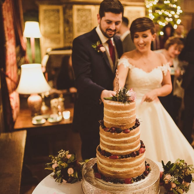 Bride &amp; Groom Cutting the Naked Wedding Cake | Burgundy &amp; Gold Winter Wedding at Ramster Hall Weddings, Surrey | Matt Penberthy Photography | John Harris Wedding Films