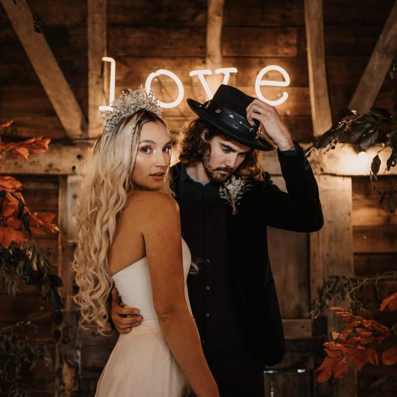 Stylish bride and groom standing in front of a LOVE neon sign