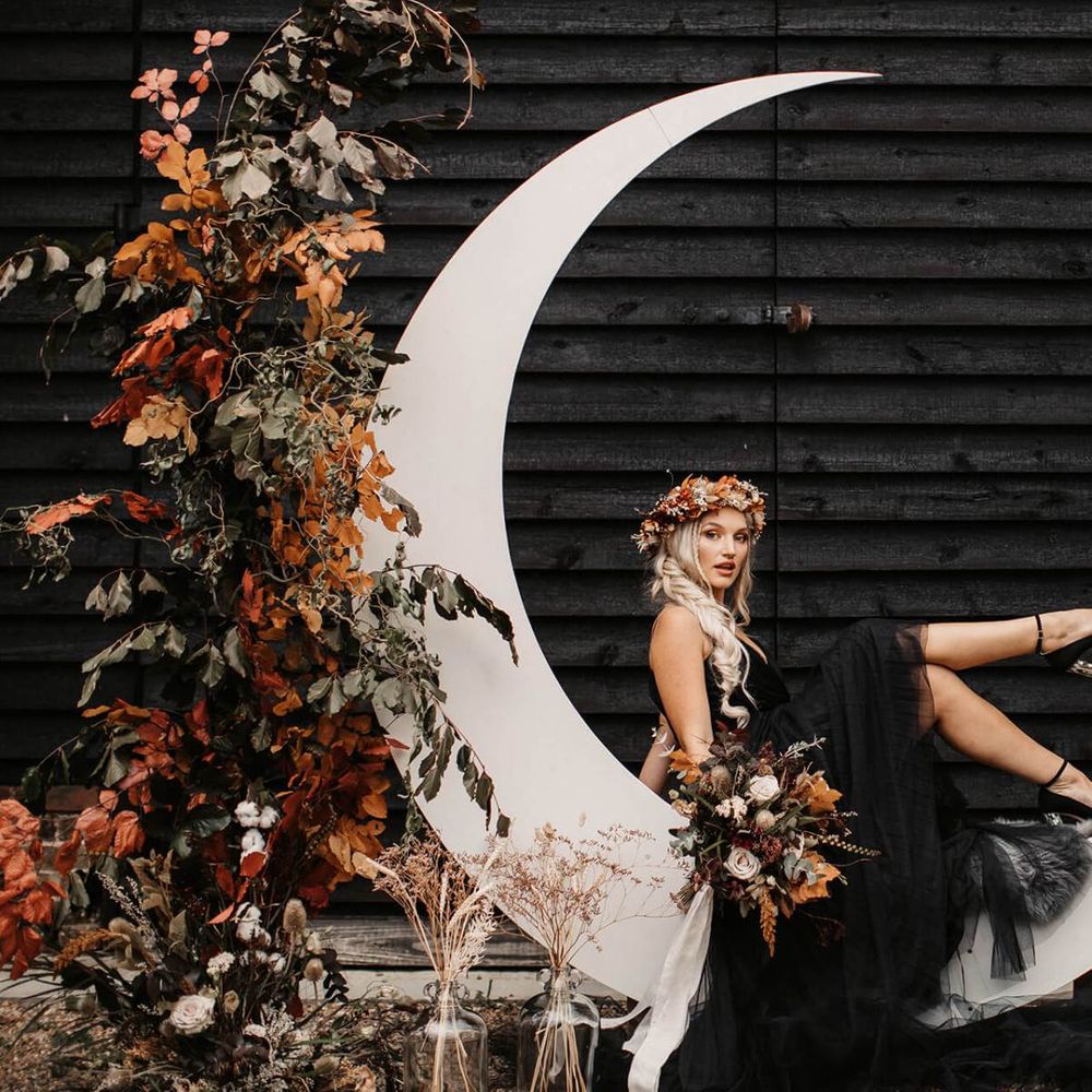 Stylish bride in black wedding dress sitting on a crescent moon  at Halloween wedding