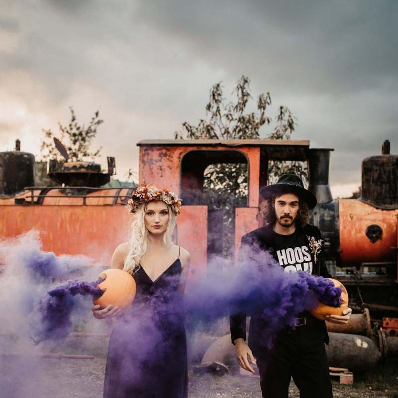 Stylish bride and groom with purple smoke bombs at Halloween wedding