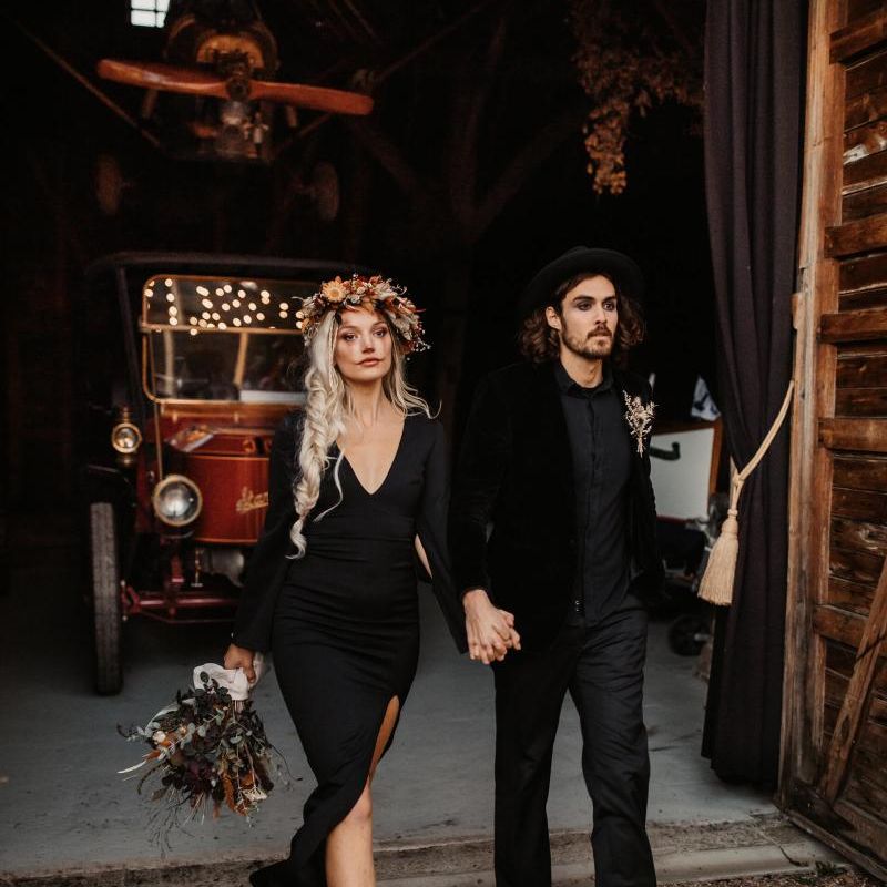 Bride in black dress with side braid and flower crown holding her grooms hand in a black shirt and hat for Halloween wedding