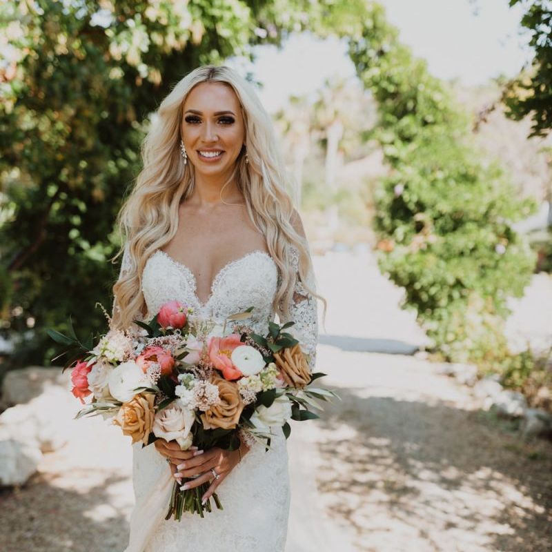 Bride walking down the aisle in a lace wedding dress holding a coral bouquet