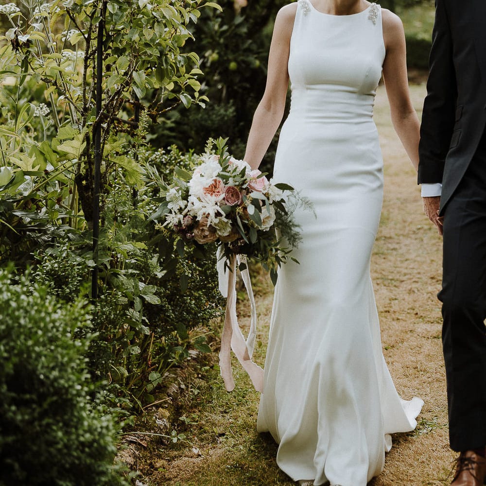 Bride in High Neck Mikaella Bridal Fitted Wedding Dress and Groom in  Clifton Suit Holding Hands