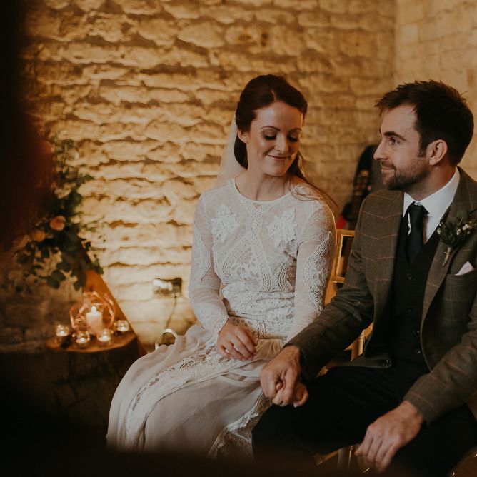 Bride in lace wedding dress and groom in wool suit holding hands