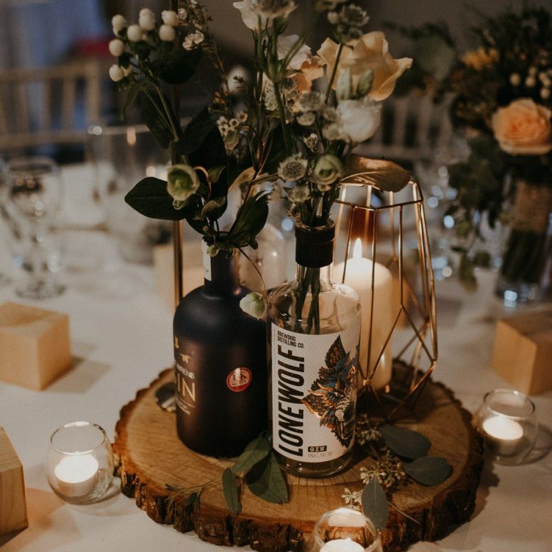Rustic centrepiece decor with tree slice, fairy lights, gin bottles and flower stems