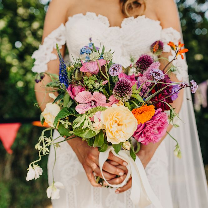 Bouquet of Bright Wild Flowers with White Ribbon | Bride in Structured Bustier Rue de Seine Fox Gown with Floral Appliqué Detail and Off The Shoulder Straps | Floor Length Veil | Colourful Bunting Wedding Decor for a Festival Themed Marquee Wedding | Peppermint Love Photography