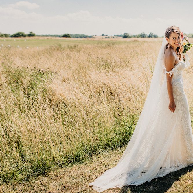 Bride in Structured Bustier Rue de Seine Fox Gown with Floral Appliqué Detail and Off The Shoulder Straps | Floor Length Veil | Rose Gold Earrings | Bouquet of Bright Wild Flowers with White Ribbon | Colourful Bunting Wedding Decor for a Festival Themed Marquee Wedding | Peppermint Love Photography