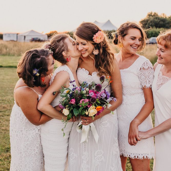 Bride in Structured Bustier Rue de Seine Fox Gown with Floral Appliqué Detail and Off The Shoulder Straps | Rose Gold Earrings | Pink Dahlia Hair Flower | Bouquet of Bright Wild Flowers with White Ribbon | Bridesmaids in White ASOS Dresses | Colourful Bunting Wedding Decor for a Festival Themed Marquee Wedding | Peppermint Love Photography