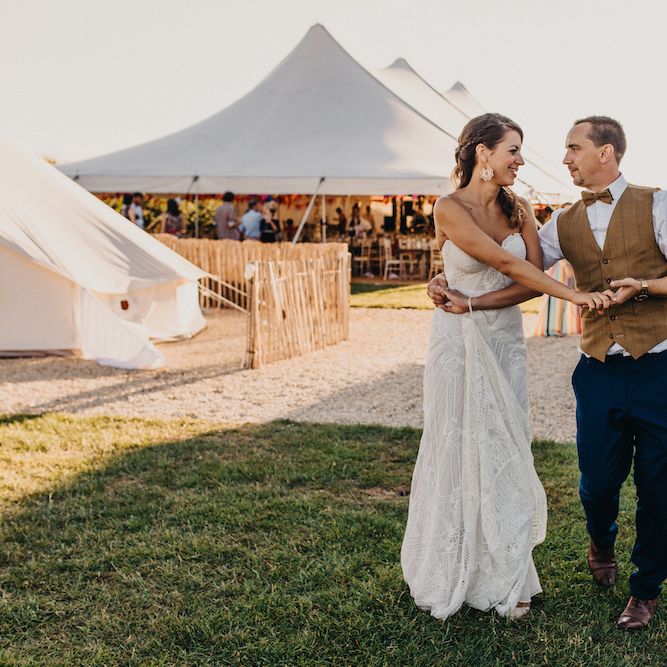 Bride in Structured Bustier Rue de Seine Fox Gown with Floral Appliqué Detail and Off The Shoulder Straps | Rose Gold Earrings | Groom in Blue Two Piece Suit with Tan Waistcoat and Bow Tie | Colourful Bunting Wedding Decor for a Festival Themed Marquee Wedding | Peppermint Love Photography