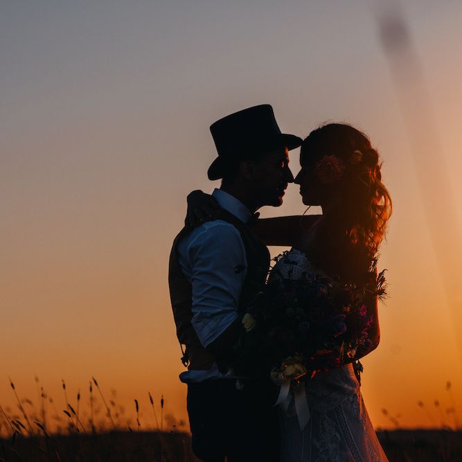 Bride in Structured Bustier Rue de Seine Fox Gown with Floral Appliqué Detail and Off The Shoulder Straps | Bouquet of Bright Wild Flowers with White Ribbon | Pink Dahlia Hair Flower | Groom in Blue Two Piece Suit with Tan Waistcoat, Bow Tie and Top Hat | Golden Hour Photo | Colourful Bunting Wedding Decor for a Festival Themed Marquee Wedding | Peppermint Love Photography