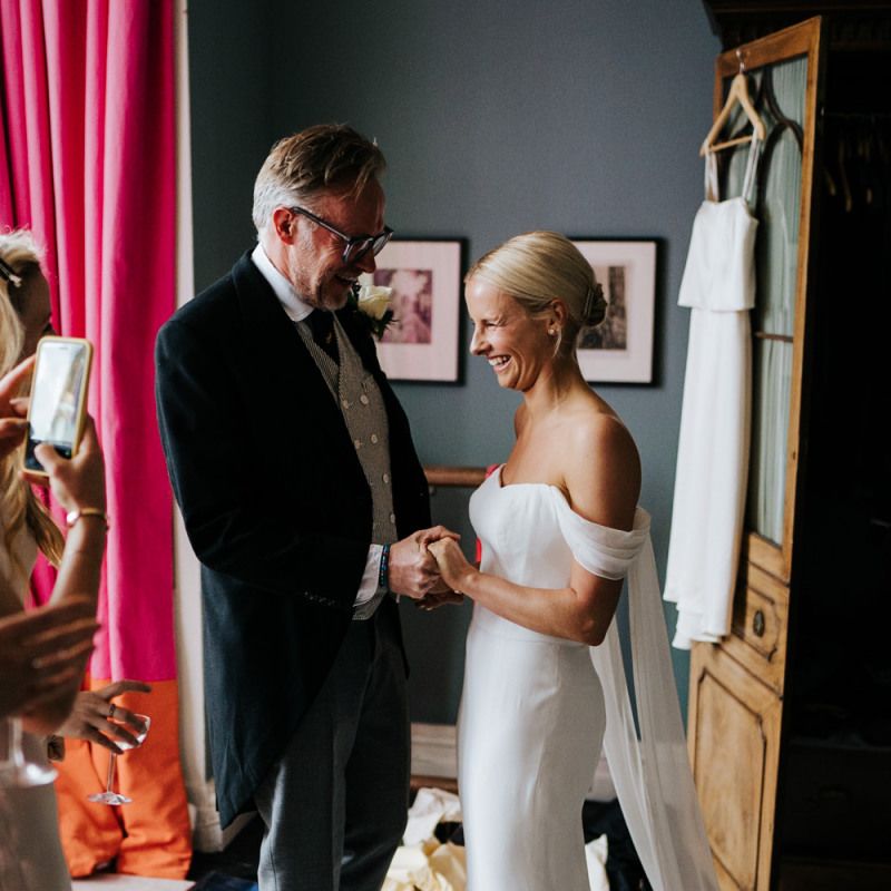 Father of the bride and bride hold hands as he sees her in her dress for the first time