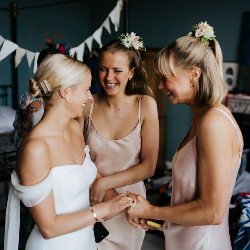 Bride holds hands and smiles at two sister in excited anticipation for the wedding ceremony