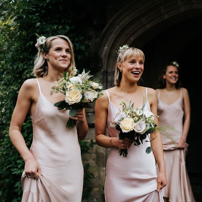 Bridesmaids hold bouquets and smile at bride, off-frame, as she enters her wedding car