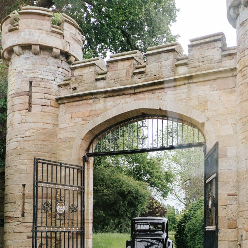 Bride's car passes under fortified gates at Hawarden Castle in Wales, UK
