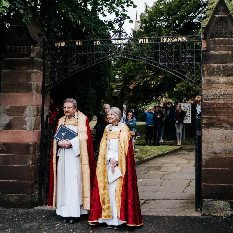 Vicars patiently await arrival of the bride outside of the village church in Hawarden, Wales