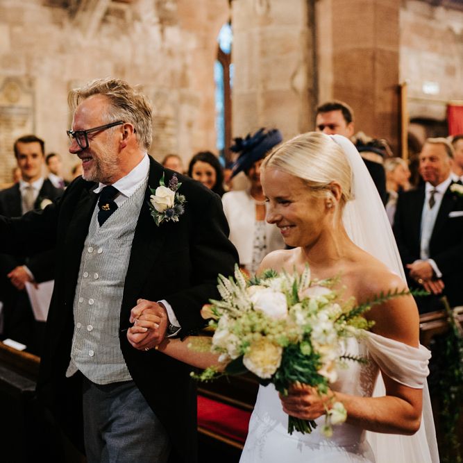 Bride and father of the bride arrive at the front of the aisle and hug the groom