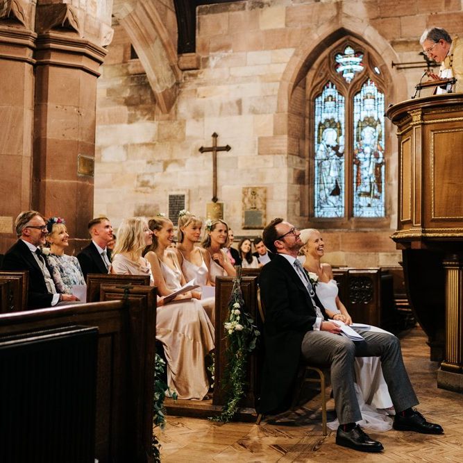 Bride and groom, and bride's family listen attentively to vicar's sermon and smile while doing so