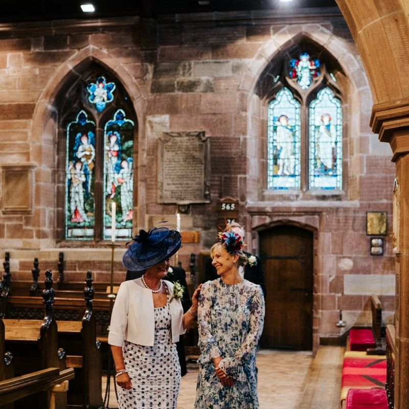 Bride and groom's mother look at each other and exchange a moment of happiness as they walk towards the signing of the register