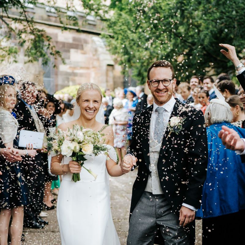 Bride and groom exit the church and walk down the pathway as guests throw confetti at them