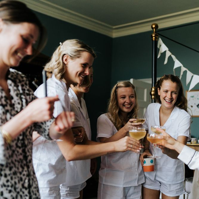 Bride and bridesmaids each hold a glass of champagne and say a toast for the day ahead