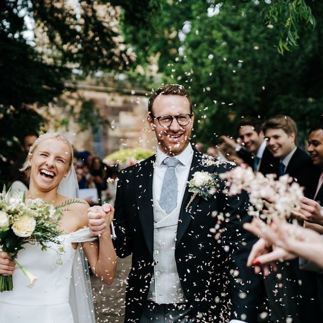 Bride and groom exit the church and walk down the pathway as guests throw confetti at them