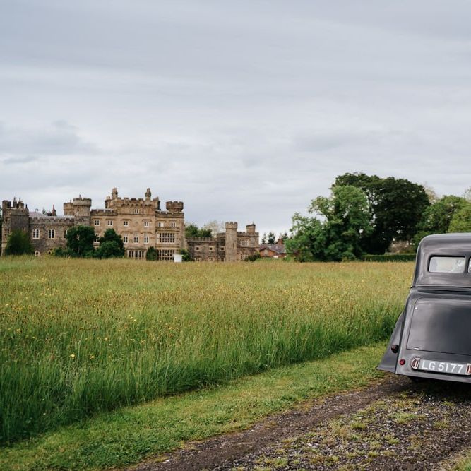 Bride and groom drive towards Hawarden Castle in beautiful, black vintage car