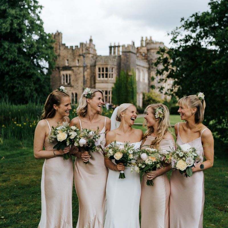 Smiling photograph of bridesmaids and bride holding bouquets with Hawarden Castle in the background