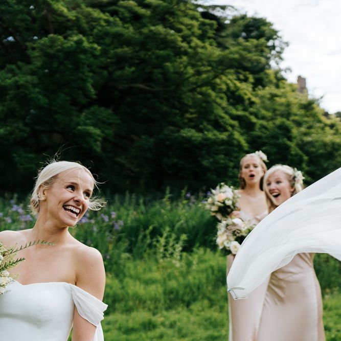 Bride's veil flies out of her hair as bridesmaids look on in amazement