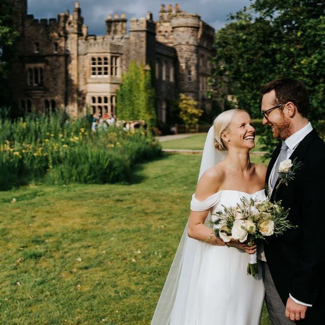 Bride in off the shoulder wedding dress and groom in traditional morning suit standing in front of Hawarden Castle in Wales