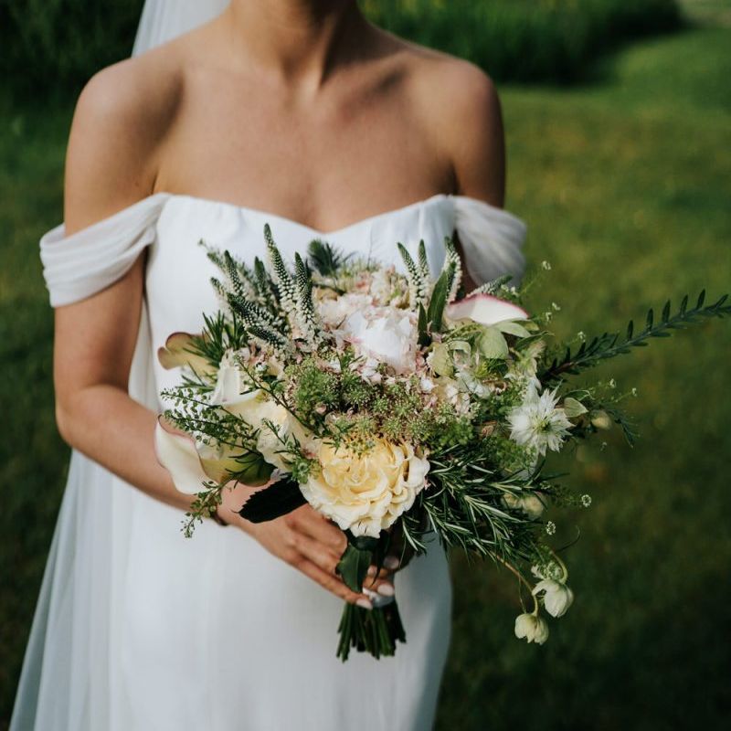 Bride in off the shoulder wedding dress holding a cream rose and foliage wedding bouquet